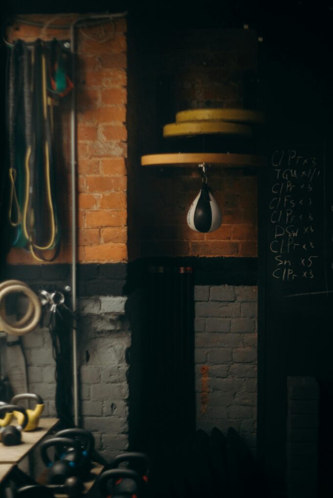 Dimly lit boxing gym interior with punching bag and workout equipment, evoking a vintage training vibe.